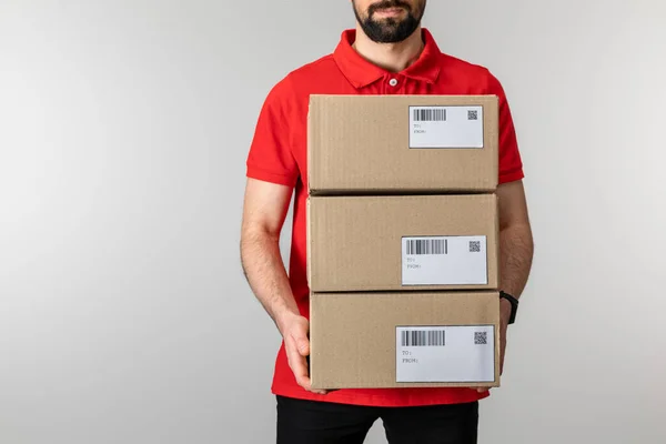 Cropped view of bearded courier holding boxes with barcodes and qr codes on cards isolated on grey — Stock Photo