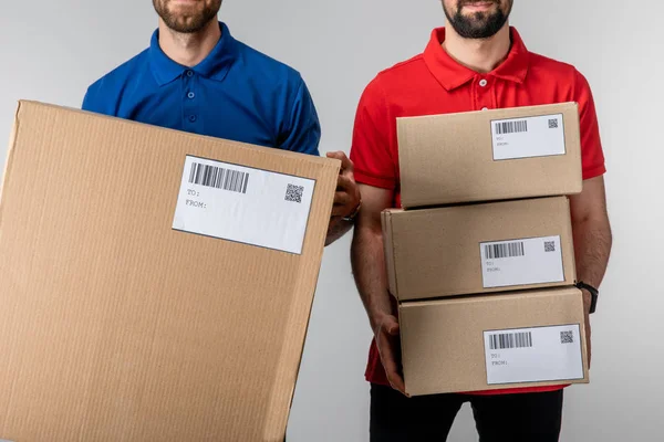Cropped view of couriers holding boxes with barcodes and qr codes on cards isolated on grey — Stock Photo