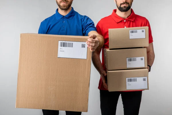 Cropped view of bearded delivery men holding boxes with barcodes and qr codes on cards isolated on grey — Stock Photo