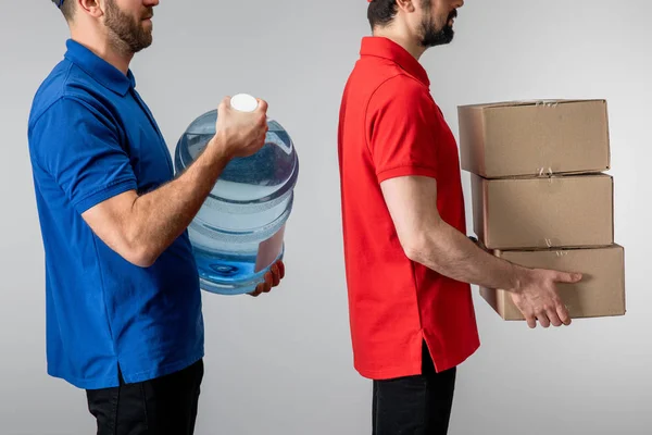 Vista lateral de correios segurando caixas de papelão e água engarrafada isolada em cinza — Fotografia de Stock