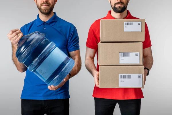 Cropped view of couriers holding cardboard packages and bottled water isolated on grey — Stock Photo
