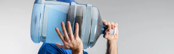 Side view of courier carrying on shoulder bottled water isolated on grey, panoramic shot — Stock Photo