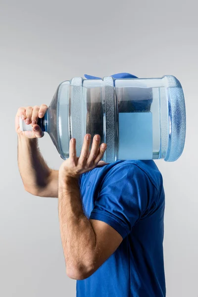 Side view of courier carrying on shoulder bottled water isolated on grey — Stock Photo