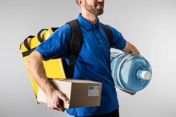 Vista recortada del repartidor con caja de sujeción de mochila térmica y agua embotellada aislada en gris - foto de stock