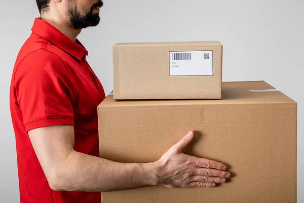 Vista lateral del mensajero que lleva cajas de cartón aisladas en gris - foto de stock