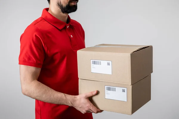 Cropped view of delivery man in uniform carrying cardboard boxes isolated on grey — Stock Photo