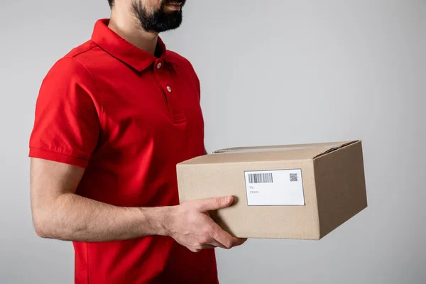 Cropped view of bearded courier in uniform carrying cardboard box isolated on grey — Stock Photo