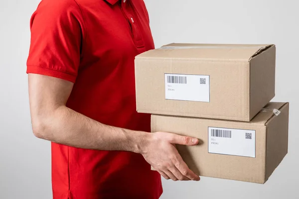 Cropped view of courier carrying cardboard packages with qr codes and barcodes on cards isolated on grey — Stock Photo