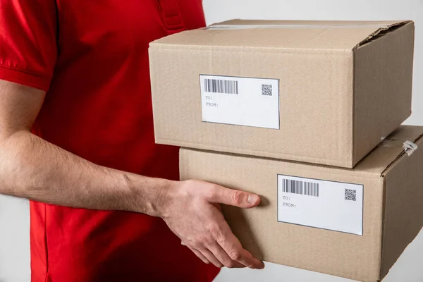 Cropped view of delivery man holding packages with qr codes and barcodes on cards isolated on grey — Stock Photo