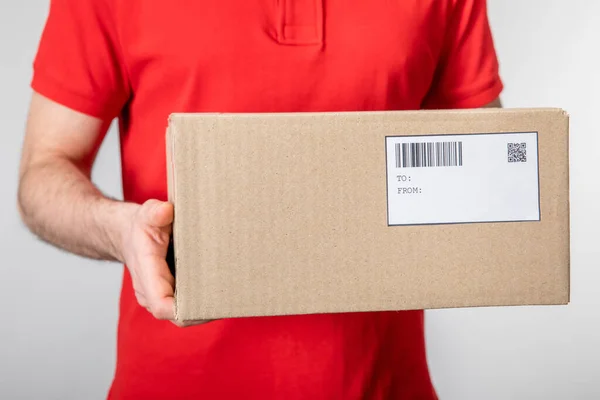 Vista cortada de correio transportando caixa de papelão com código de barras e código qr no cartão isolado em cinza — Fotografia de Stock