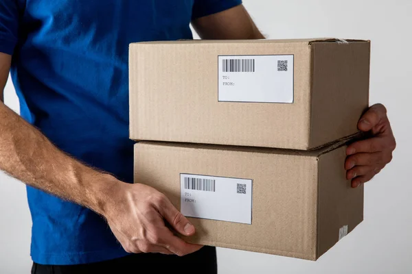 Cropped view of courier holding boxes with barcodes and qr codes on cards isolated on grey — Stock Photo