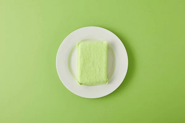Вид зверху на білу тарілку і губку для миття посуду на зеленому — стокове фото