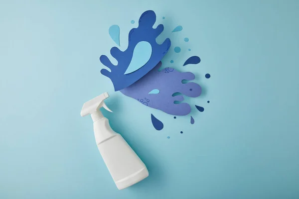 Composição vista superior com frasco de spray e respingos de água azul feitos de papel, em azul — Fotografia de Stock