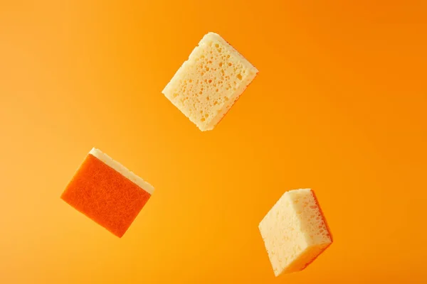Желтые падающие губки для мытья посуды изолированы на оранжевый — стоковое фото
