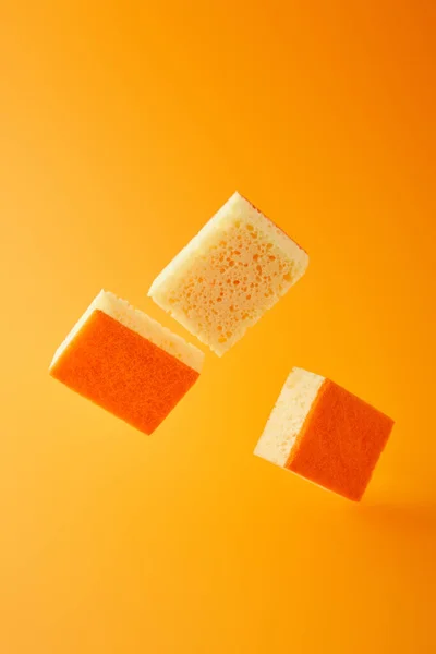 Желтые падающие губки для мытья посуды изолированы на оранжевый — стоковое фото