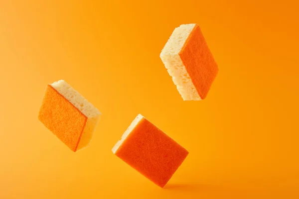 Три падающих губки для мытья посуды на апельсине — стоковое фото