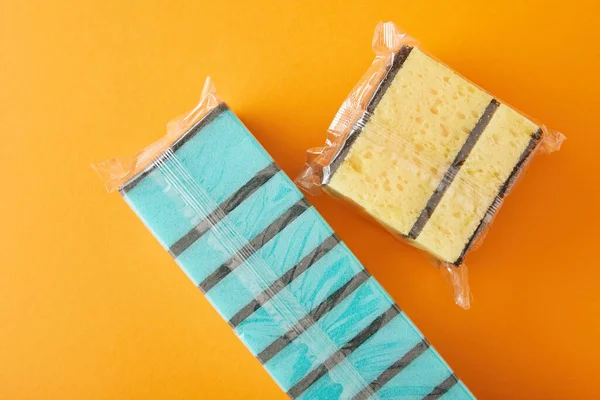 Ansicht von verpackten blauen und gelben Schwämmen für die Hausreinigung auf orange — Stockfoto