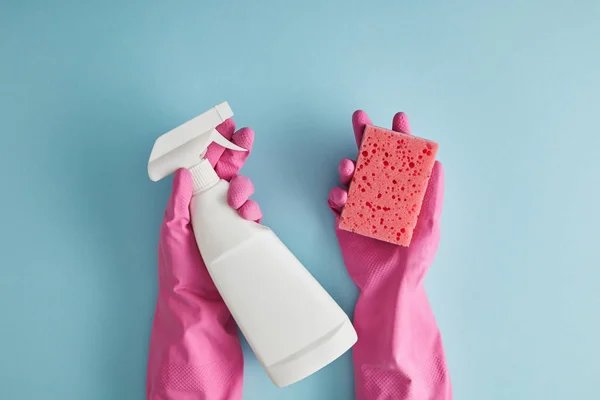 Vista recortada de la ama de llaves en guantes de goma rosa con esponja y botella de spray en azul - foto de stock