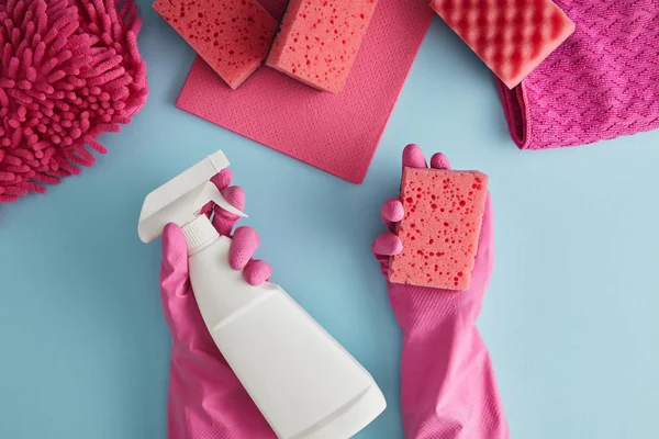 Cropped view of housekeeper in pink rubber gloves holding sponge and spray bottle on blue with rags — Stock Photo