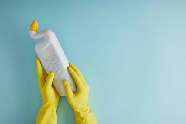 Cropped view of housekeeper in yellow rubber gloves holding bottle with toilet cleaner on blue — Stock Photo