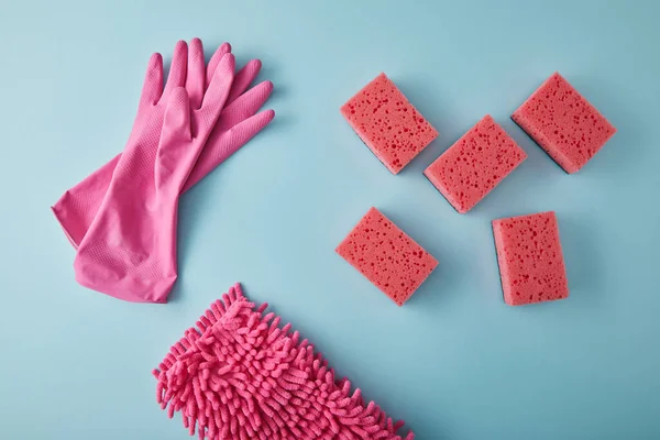 Vista superior de guantes de goma rosa, trapo y esponjas para la limpieza de la casa en azul - foto de stock