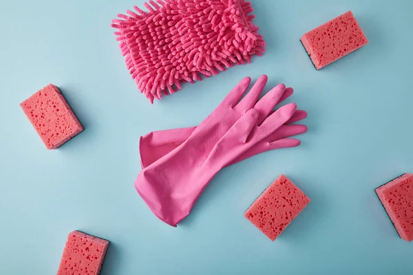 Vista superior de pano rosa, luvas de borracha e esponjas para limpeza da casa em azul — Fotografia de Stock