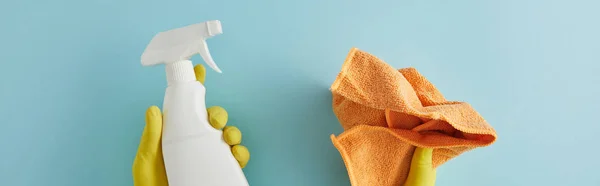 Panoramic shot of housekeeper in rubber gloves holding spray bottle and rag on blue — Stock Photo