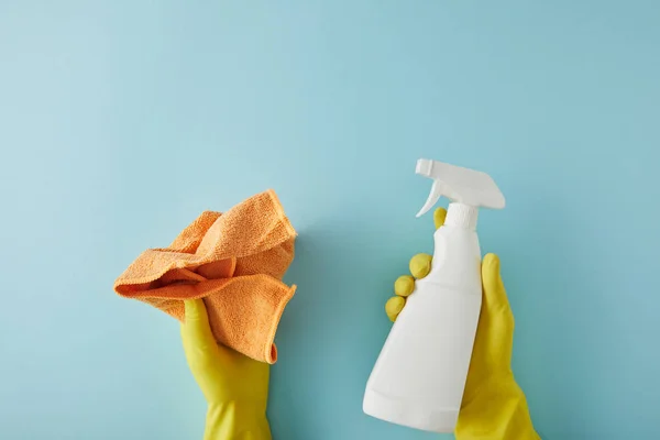 Cropped view of housekeeper in yellow rubber gloves holding spray bottle and rag on blue — Stock Photo