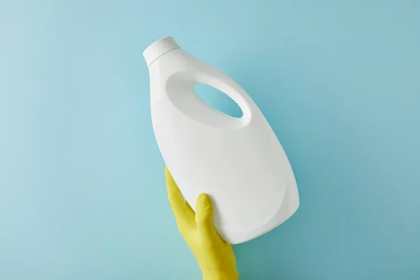 Cropped view of housekeeper in rubber glove holding bottle with cleaning product on blue — Stock Photo