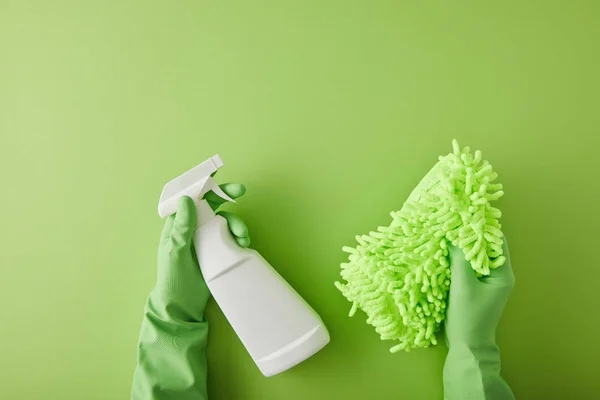 Top view of housekeeper in rubber gloves holding spray bottle and rag on green — стоковое фото
