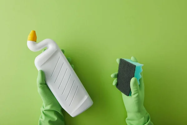 Vista recortada de la ama de llaves en guantes de goma que sostienen la esponja y la botella con limpiador de inodoro en verde - foto de stock
