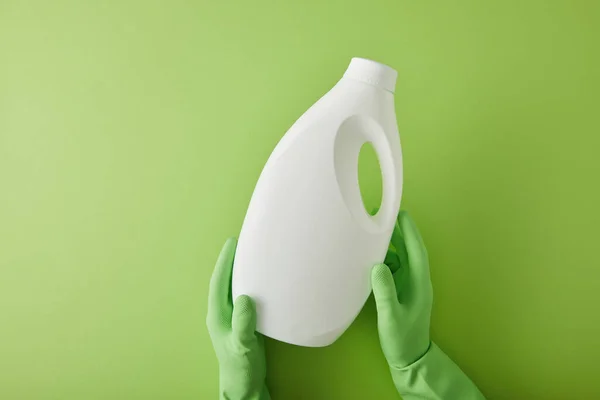 Top view of housekeeper in rubber gloves holding bottle with cleaning product on green — Stock Photo