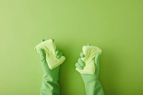 Cropped view of housekeeper in rubber gloves holding two sponges on green — Stock Photo