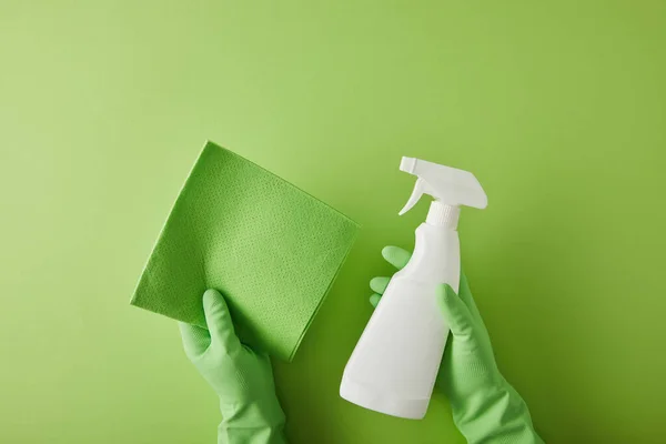 Top view of housekeeper in rubber gloves holding rag and spray bottle on green — Stock Photo