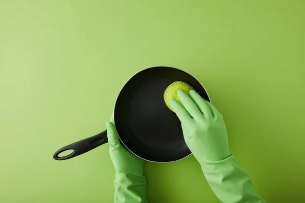 Vista recortada de ama de llaves en guantes de goma lavando sartén con esponja en verde - foto de stock