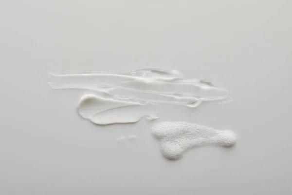 Vue de dessus des coups de pinceau gel et crème cosmétique avec mousse de savon sur fond gris — Photo de stock