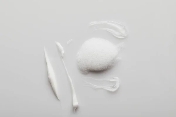 Vue de dessus des coups de pinceau gel et crème cosmétique avec mousse de savon sur fond gris — Photo de stock