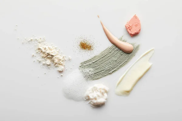 Vue de dessus des coups de pinceau visage poudre, argile, cosmétique et crème tonique avec mousse savonneuse, blusher et étincelles dorées sur fond gris — Photo de stock