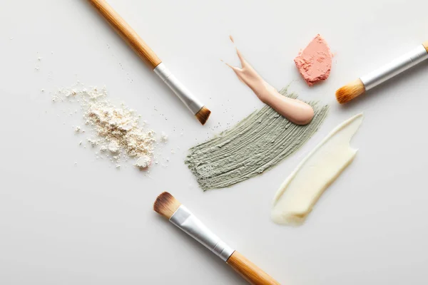 Top view of face powder, clay, cosmetic and tone cream brushstrokes, brushes and blusher on grey background — Stock Photo