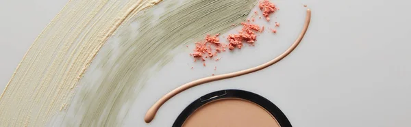 Top view of tone cream and cosmetic clay brushstrokes with face powder and blusher on grey, panoramic shot — Stock Photo