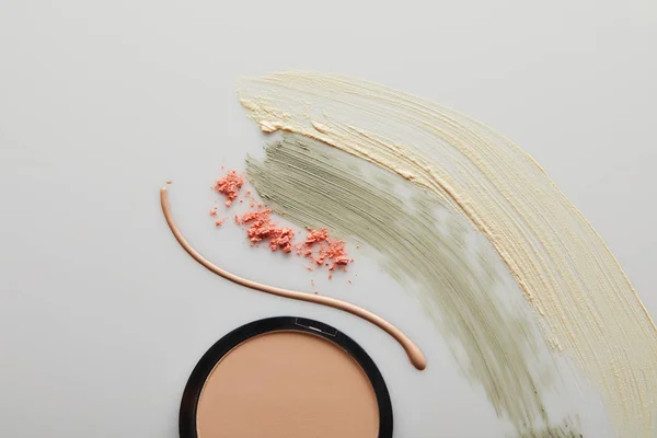 Top view of tone cream and cosmetic clay brushstrokes with face powder and blusher on grey — Stock Photo