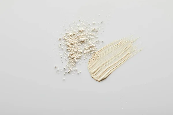 Top view of tone cream brushstrokes and face powder on grey background — Stock Photo
