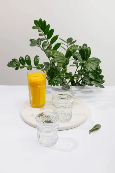 Glass of delicious yellow smoothie on white surface near green peace lily plant isolated on grey — Stock Photo