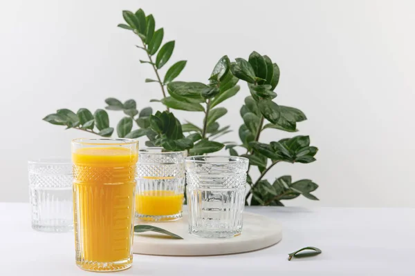 Glas leckerer gelber Smoothie auf weißer Oberfläche in der Nähe grüner Pflanzen isoliert auf grau — Stockfoto
