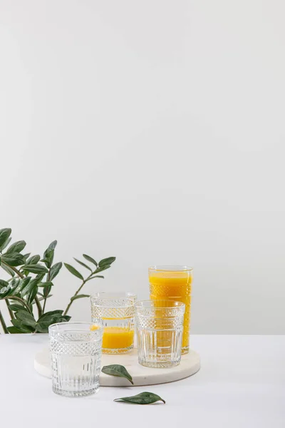 Verres de délicieux smoothie jaune sur surface blanche près de la plante verte isolée sur gris — Photo de stock