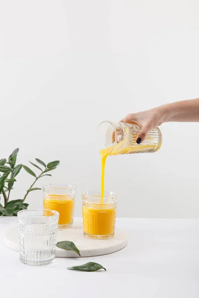 Cropped view of woman pouring delicious yellow smoothie in glass near green plant isolated on white — Stock Photo