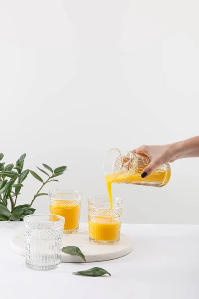 Vista recortada de la mujer vertiendo delicioso batido amarillo en vidrio cerca de la planta verde aislado en blanco - foto de stock