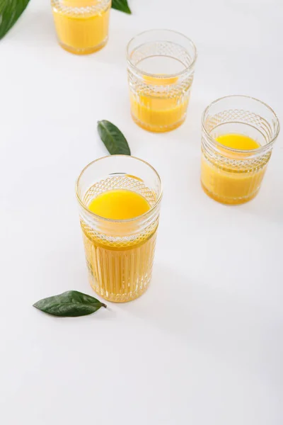 Bicchieri di delizioso frullato giallo fresco su superficie bianca con foglie verdi — Foto stock
