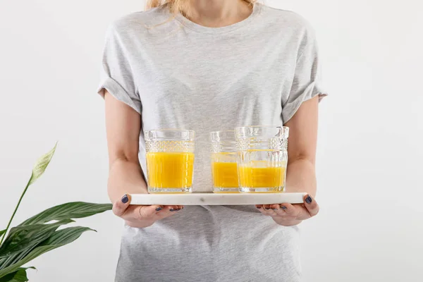 Vista recortada de la mujer sosteniendo bandeja con vasos de batido amarillo delicioso fresco cerca de la planta de lirio de paz verde aislado en blanco - foto de stock