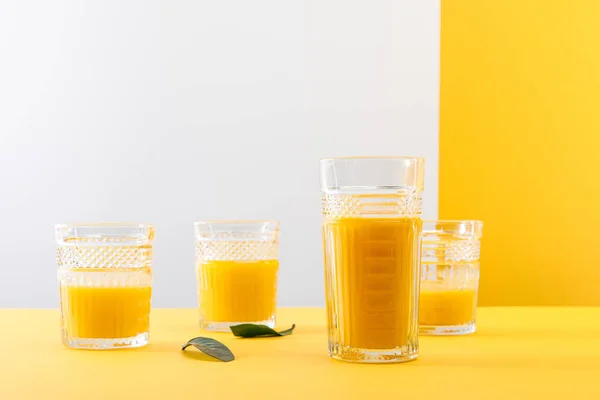 Bicchieri di fresco delizioso frullato giallo vicino a foglie verdi — Foto stock